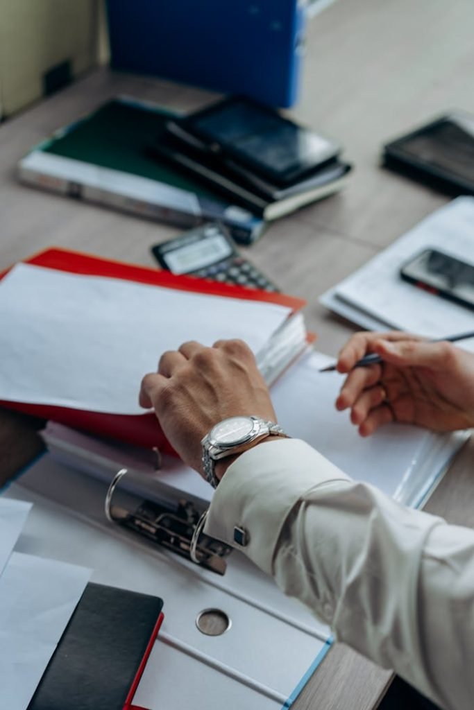Businessmans hands organizing paperwork and files on a busy office desk.