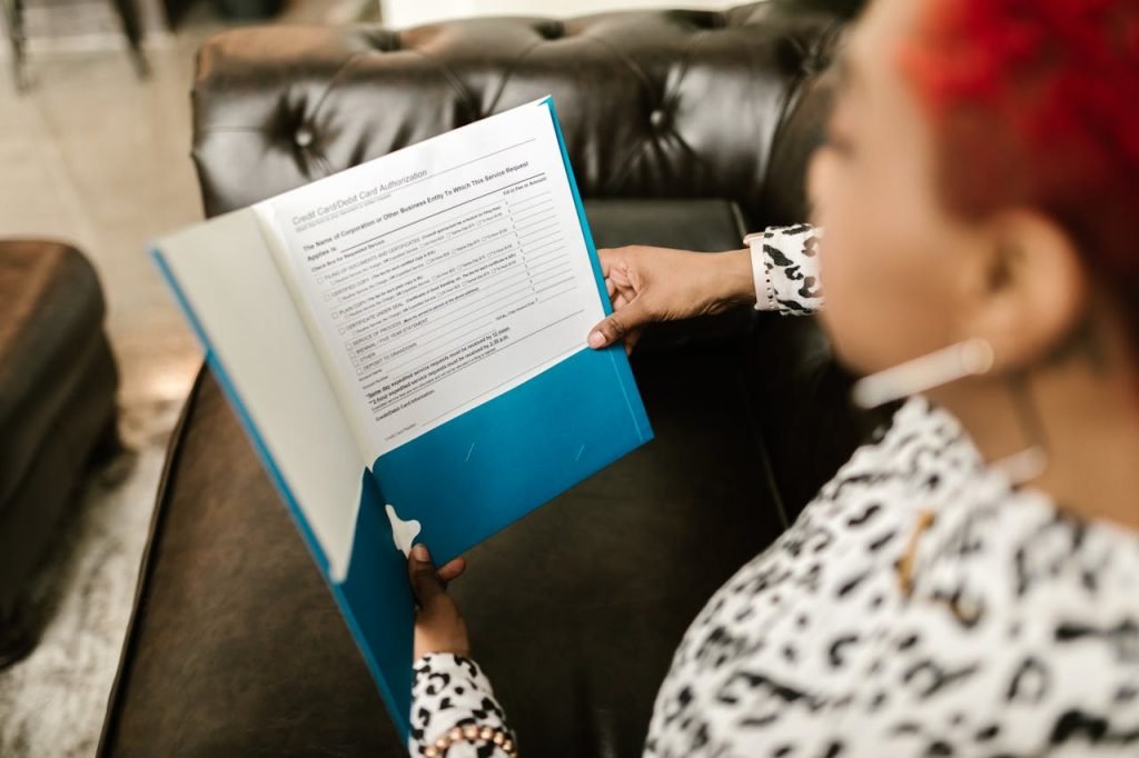 A woman sits on a couch reading a document in a blue folder.